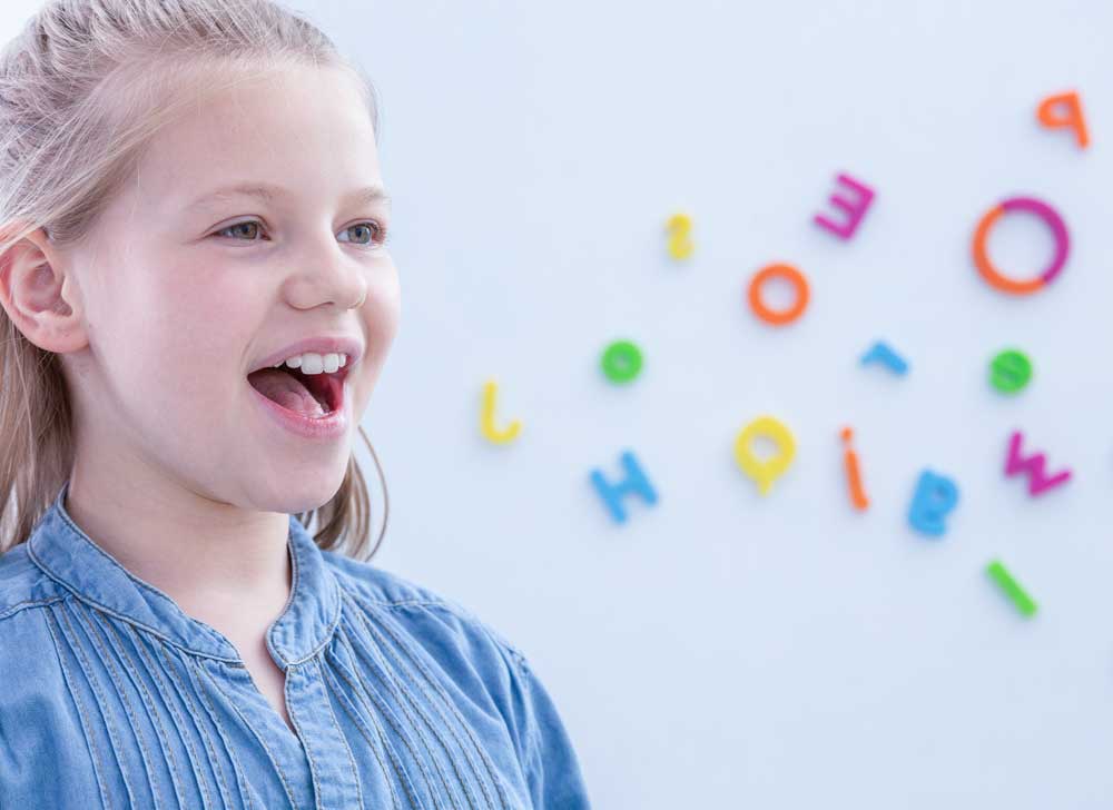 Cute blond little girl opening her mouth during speech therapy, copy space on the wall with letters von Photographee.eu AdobeStock_285103269_Web